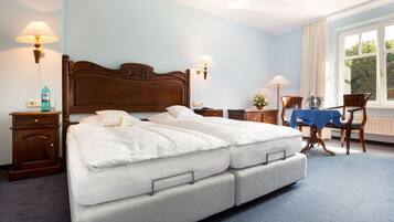A hotel room with a large bed, two bedside tables, a desk with a chair, and a window with curtains.