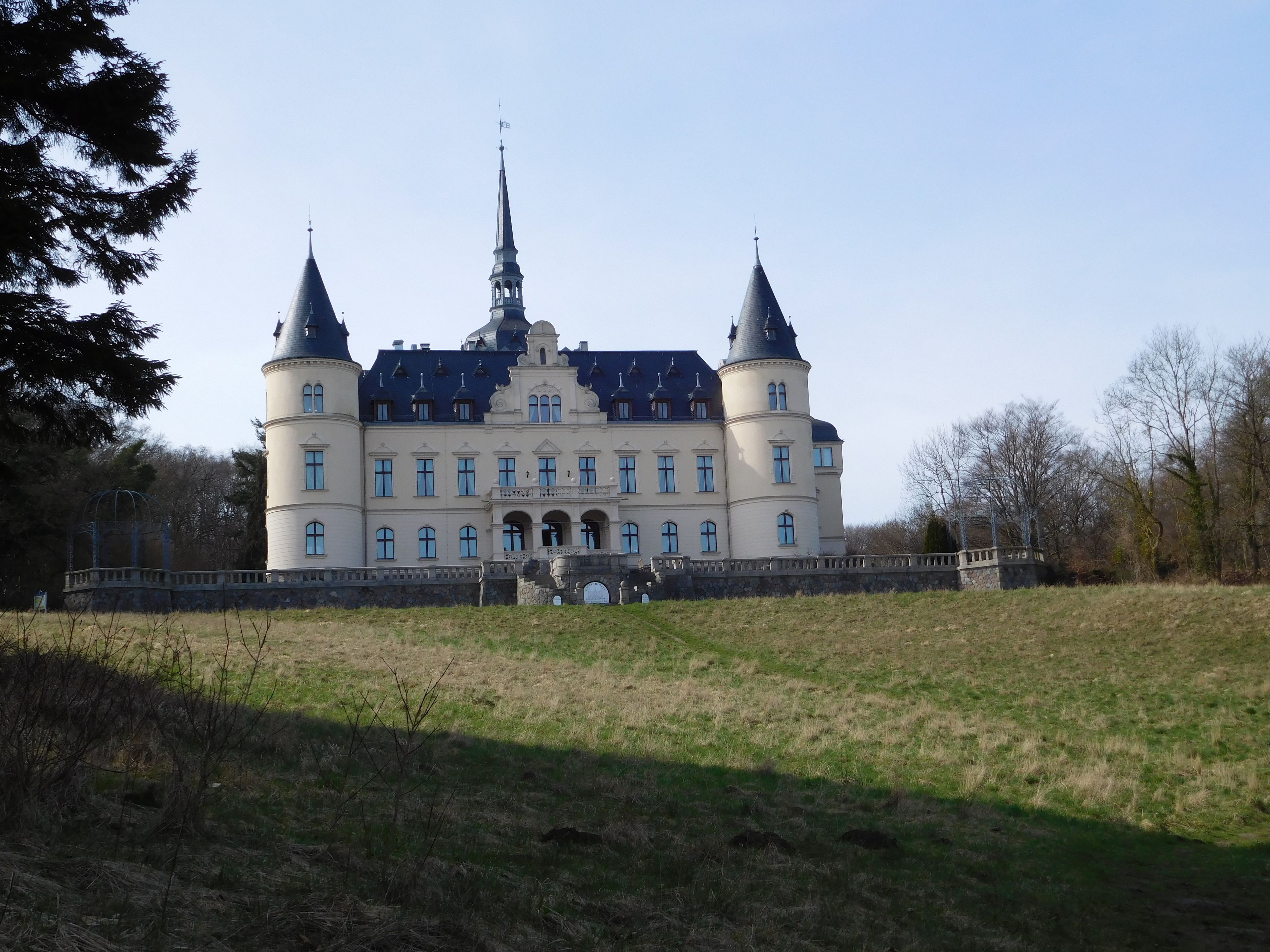 A large, historic building with a central tower and two smaller towers, surrounded by a grassy area and trees.