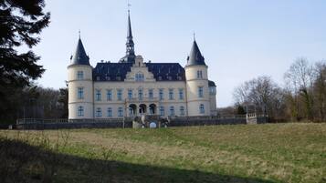 A large, historic building with a central tower and two smaller towers, surrounded by a grassy area and trees.