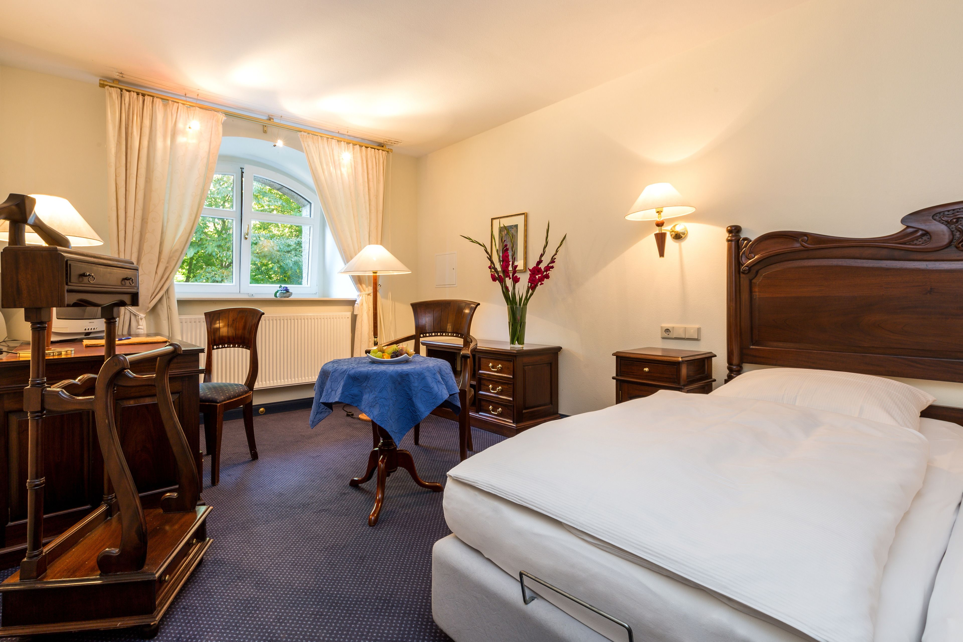 A hotel room with a bed, desk, chair, lamp, and window with curtains.