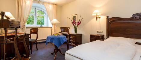 A hotel room with a bed, desk, chair, lamp, and window with curtains.