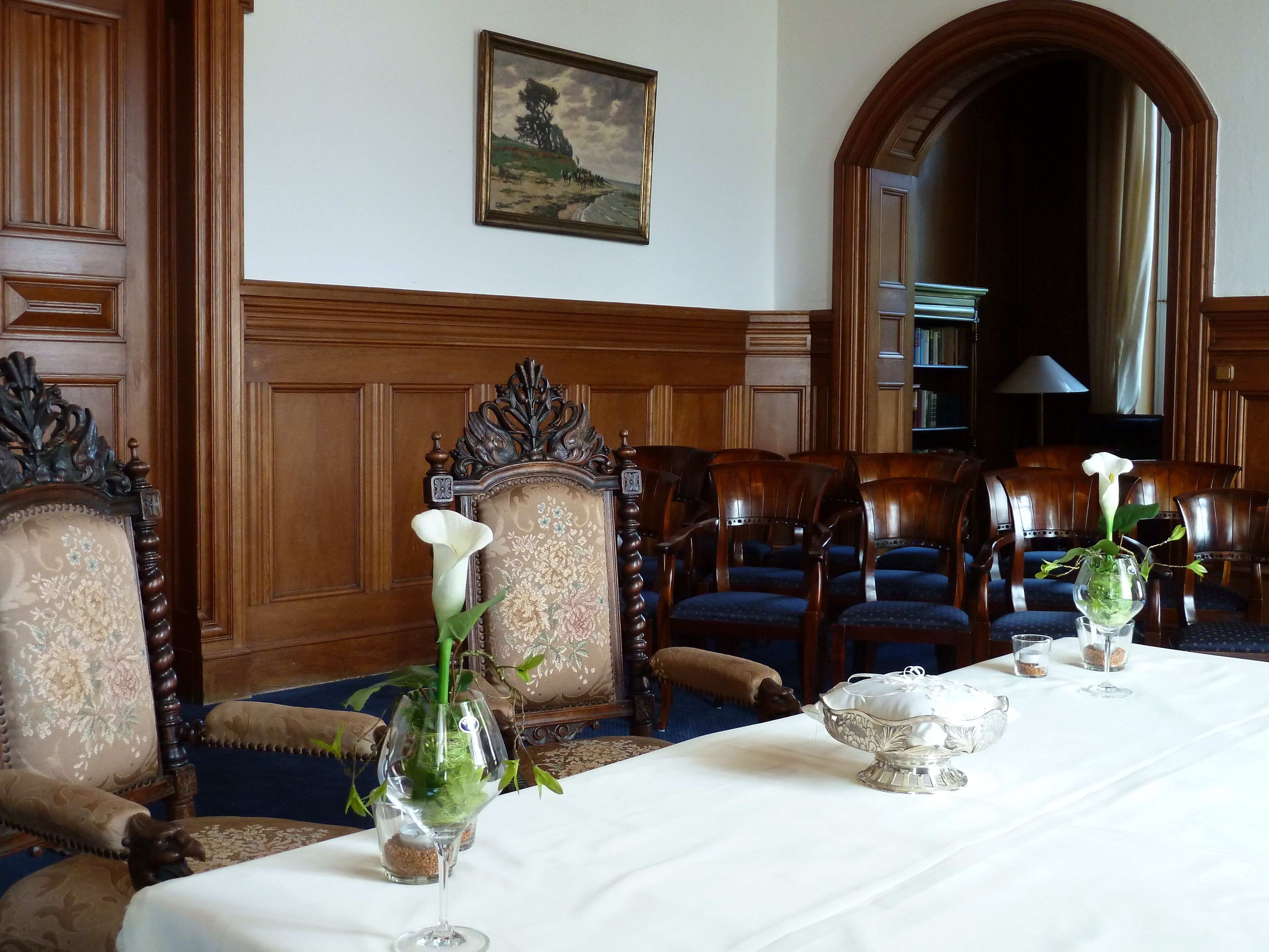 A formal dining room with a long table, elegant chairs, and a painting on the wall.