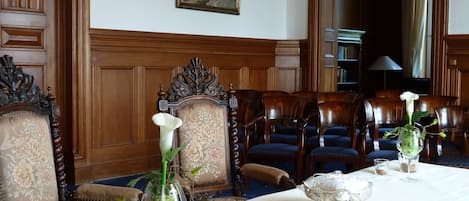 A formal dining room with a long table, elegant chairs, and a painting on the wall.