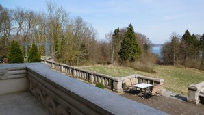 A stone balustrade overlooking a grassy area with a view of trees and a body of water. - Schlosshotel Ralswiek (Ralswiek)