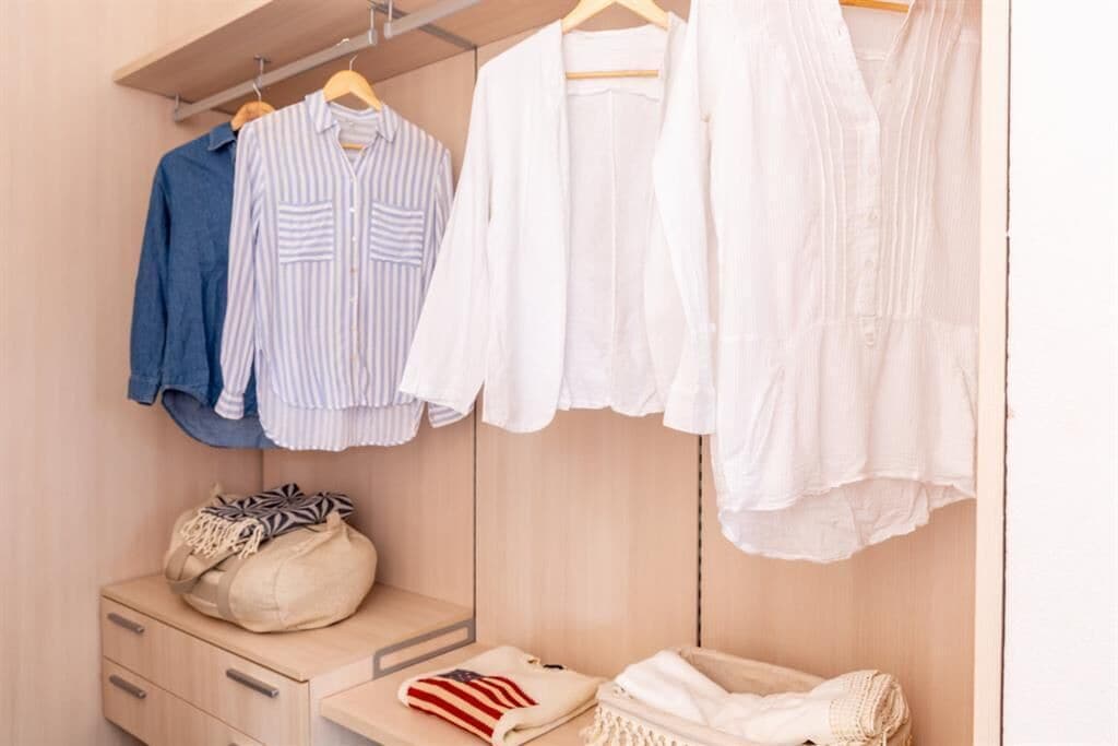 A closet with hanging clothes, a wooden dresser, and a bag.