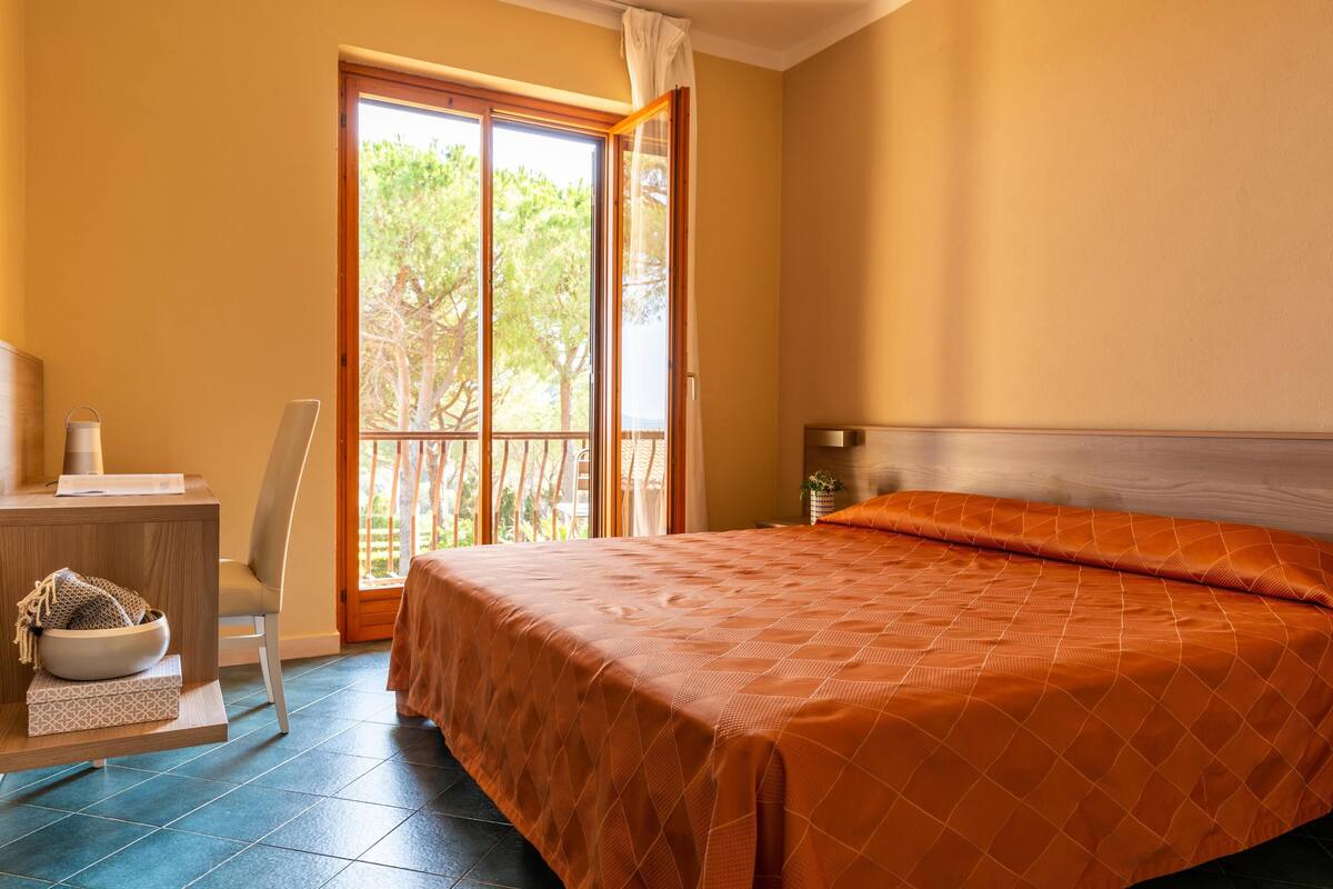 Una habitación con cama, escritorio y ventana con vistas a árboles.