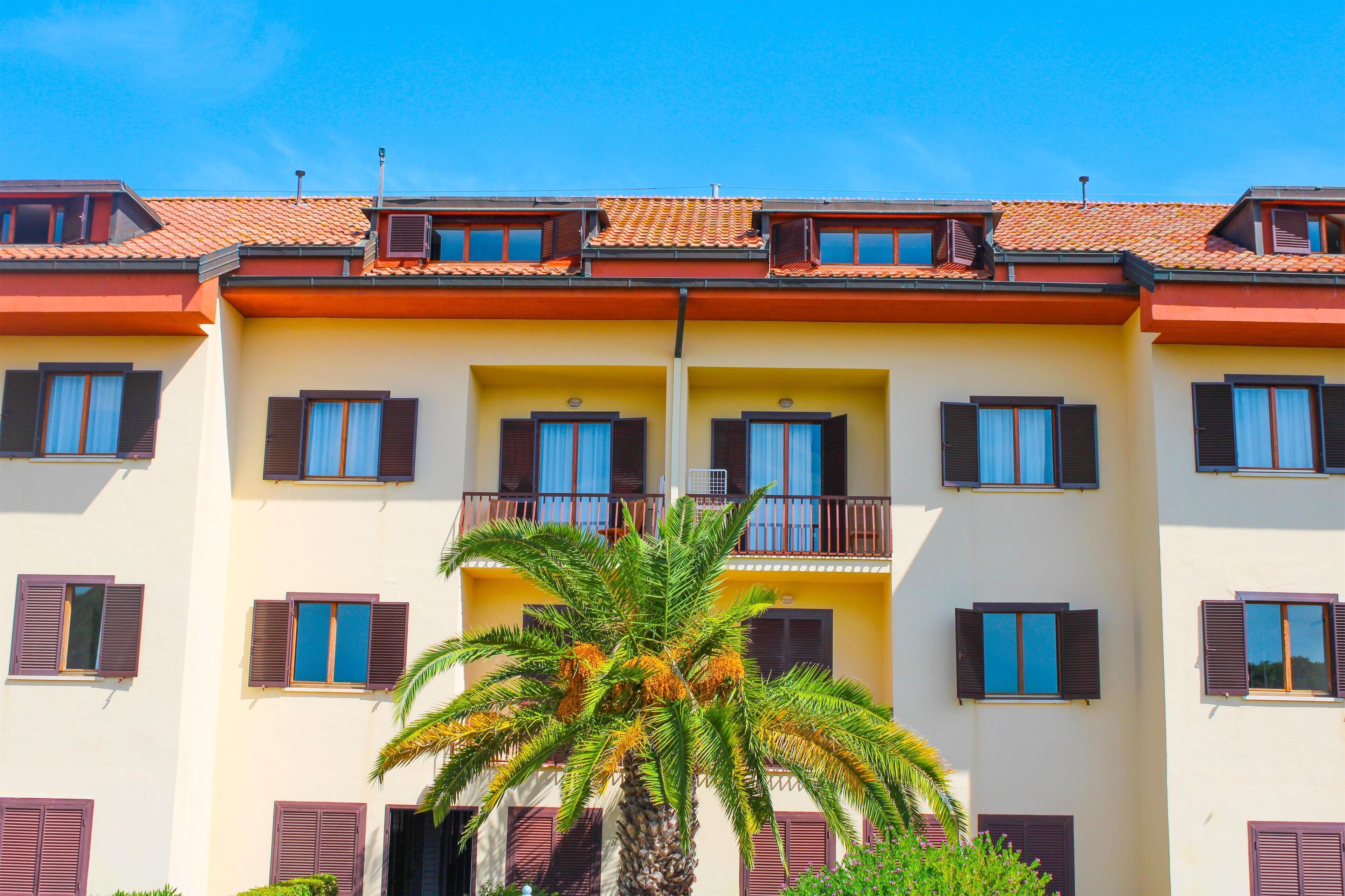 Un edificio a più piani con balconi, una palma sullo sfondo e un cielo azzurro limpido.