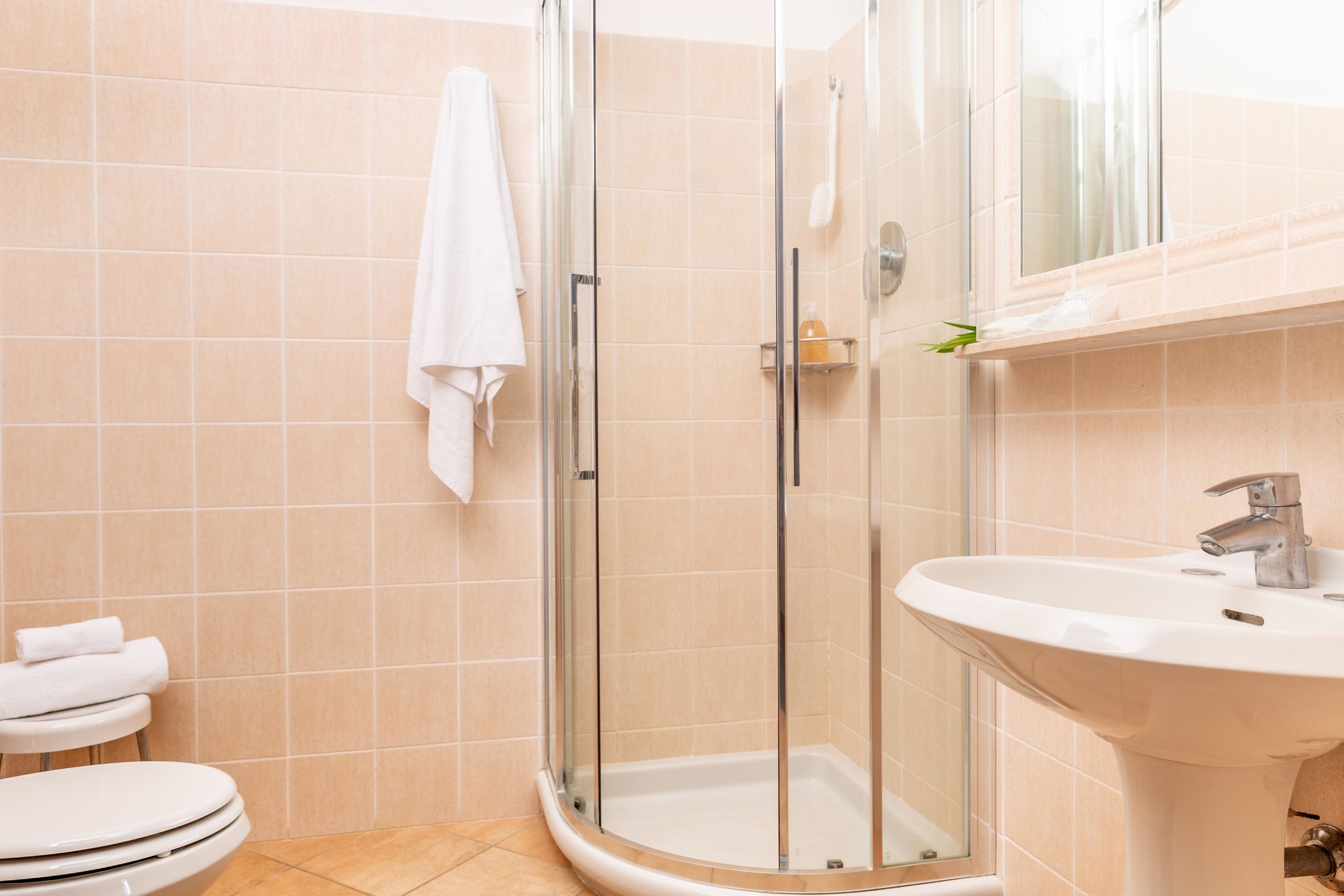 Un baño con ducha envuelta en vidrio, un lavamanos blanco y un inodoro.