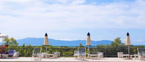 Zona de piscina con sillones de descanso y sombrillas, cielo despejado y montañas al fondo.