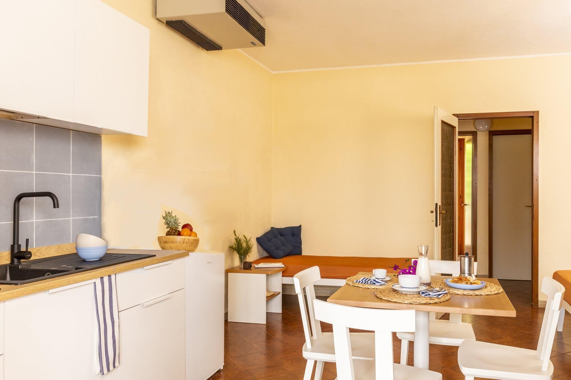 A compact kitchen with a sink, stove, and a bowl of fruit on the counter.