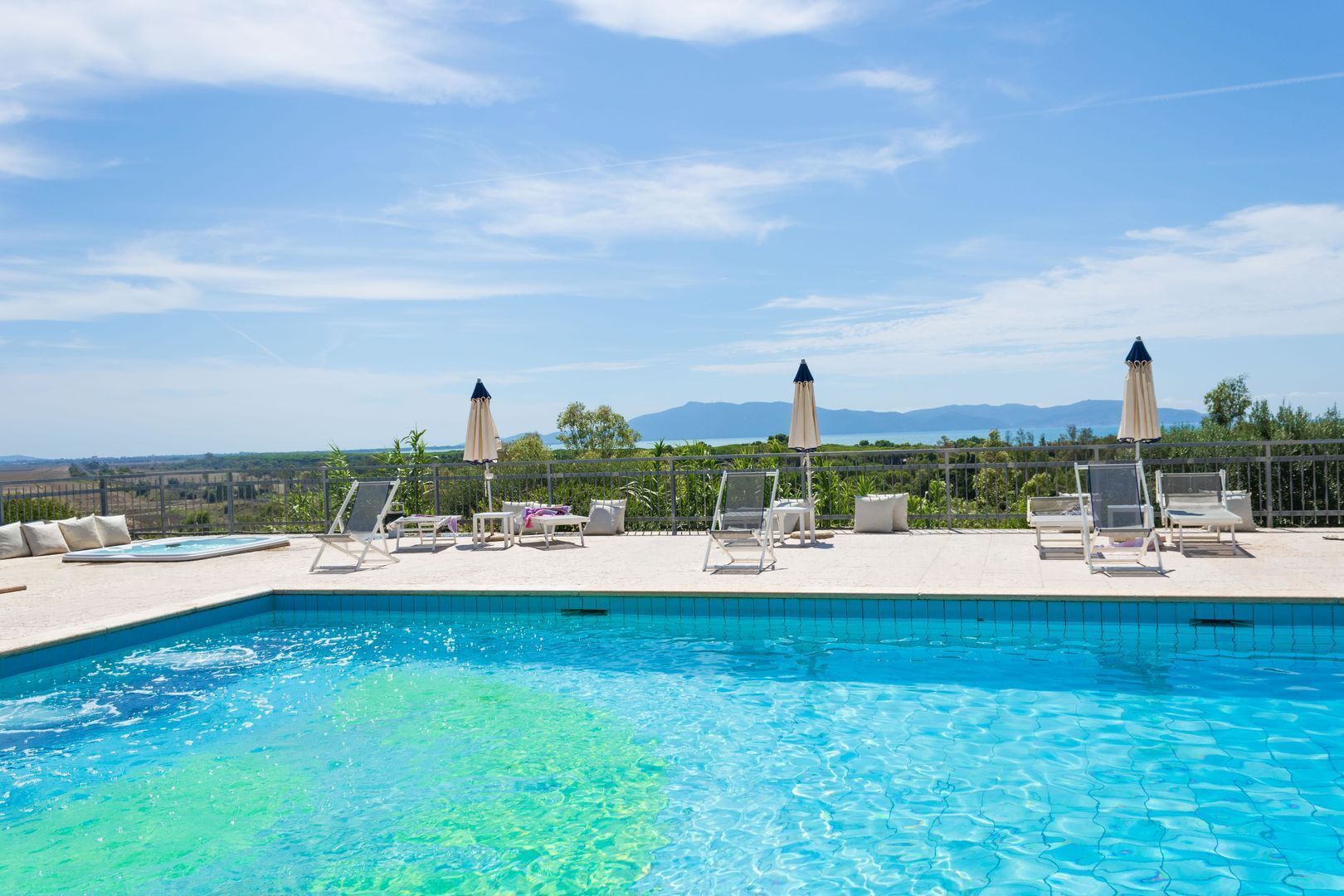 A pool with clear blue water, surrounded by lounge chairs and umbrellas, with a view of distant mountains.