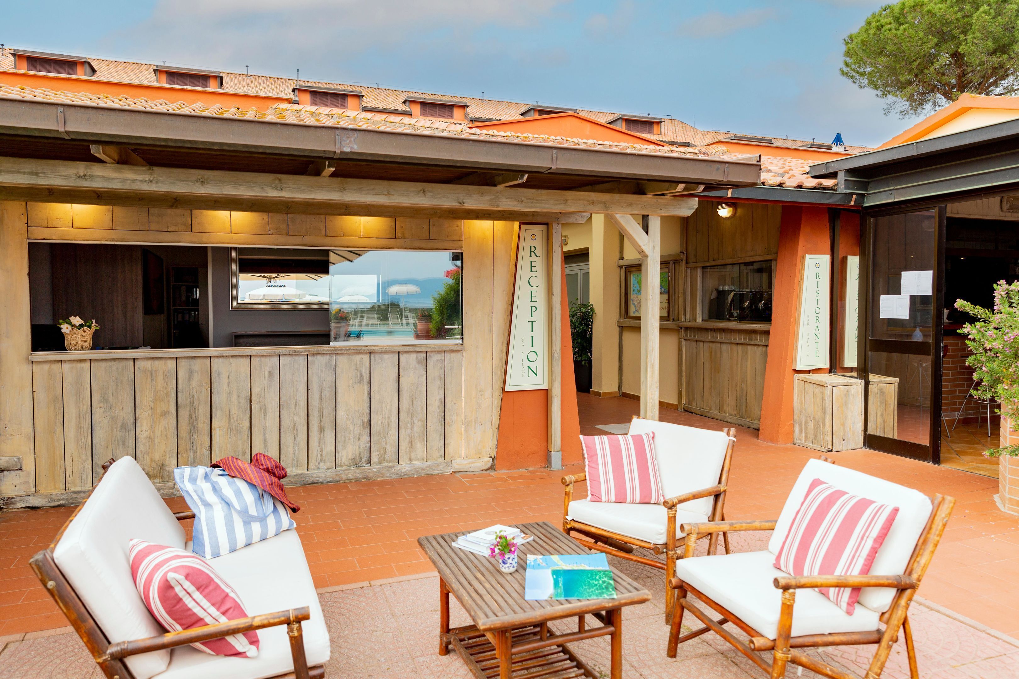 Un área de estar exterior con sillas de mimbre y una mesa de madera, una recepción y vistas al mar.