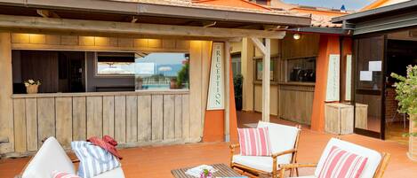 Un área de estar exterior con sillas de mimbre y una mesa de madera, una recepción y vistas al mar.