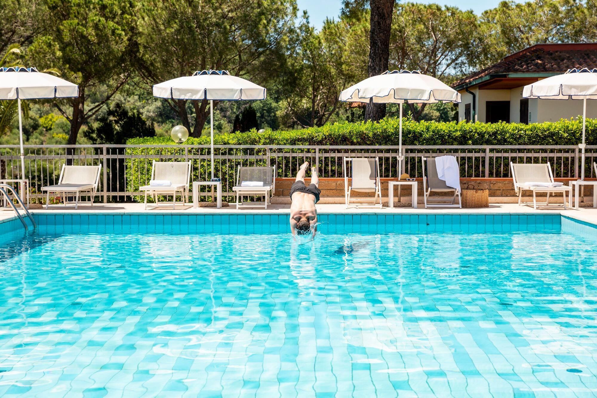 A swimming pool with lounge chairs and umbrellas, surrounded by trees and a fence.