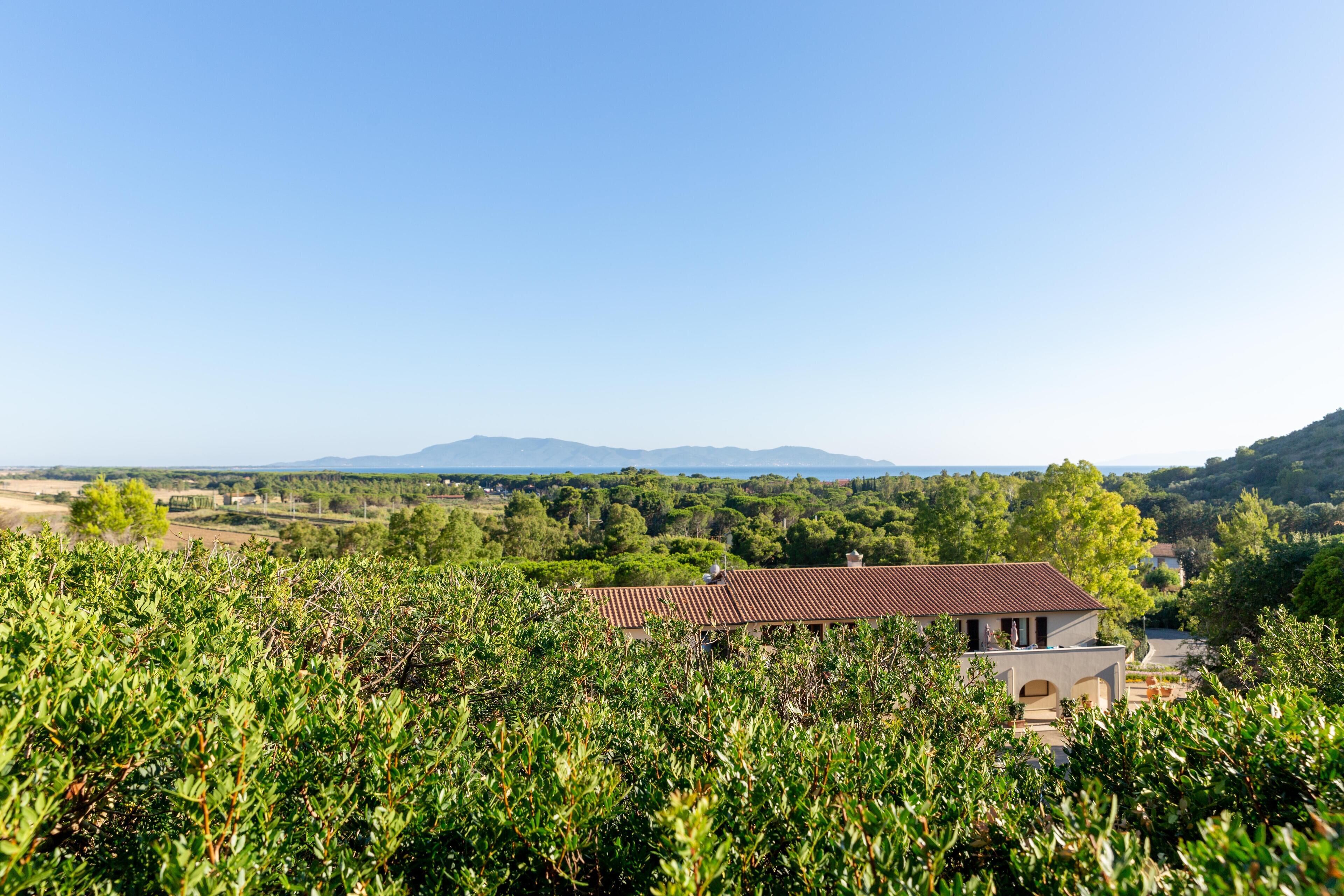 A house with a red roof surrounded by lush greenery and distant mountains.