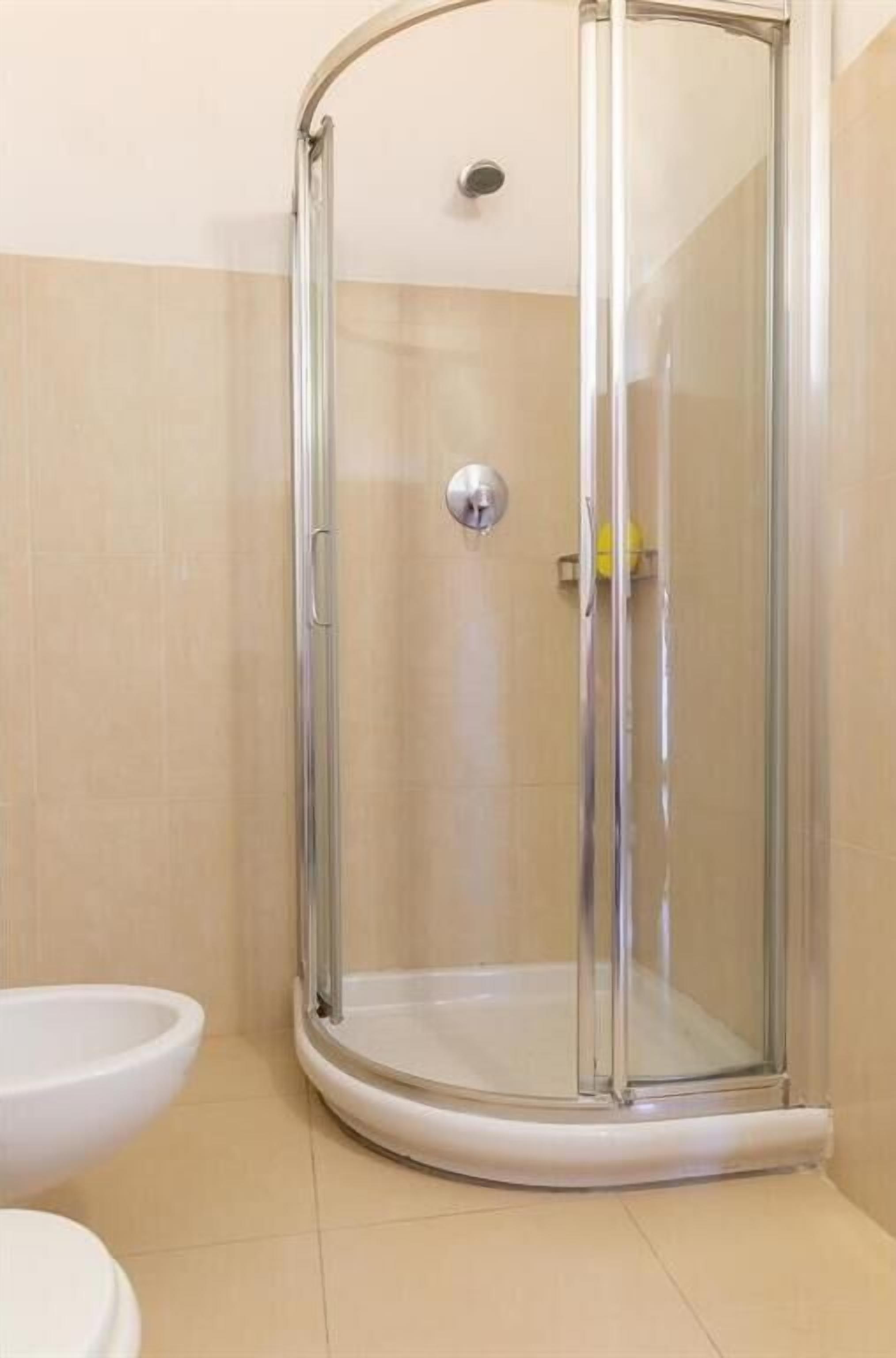 Une douche d’angle avec une porte en verre, un lavabo blanc et des toilettes.