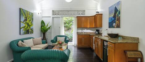 A spacious room with a high ceiling, a dining area with a wooden table, green wicker furniture, and a kitchen area with wooden cabinets and a countertop.