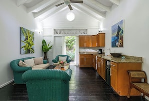A spacious room with a high ceiling, a dining area with a wooden table, green wicker furniture, and a kitchen area with wooden cabinets and a countertop.