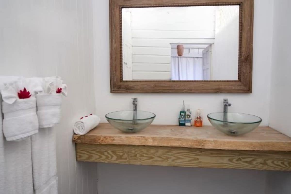 Une salle de bain avec deux vasques en verre, un plan de toilette en bois, un miroir et un porte-serviettes avec des serviettes blanches.
