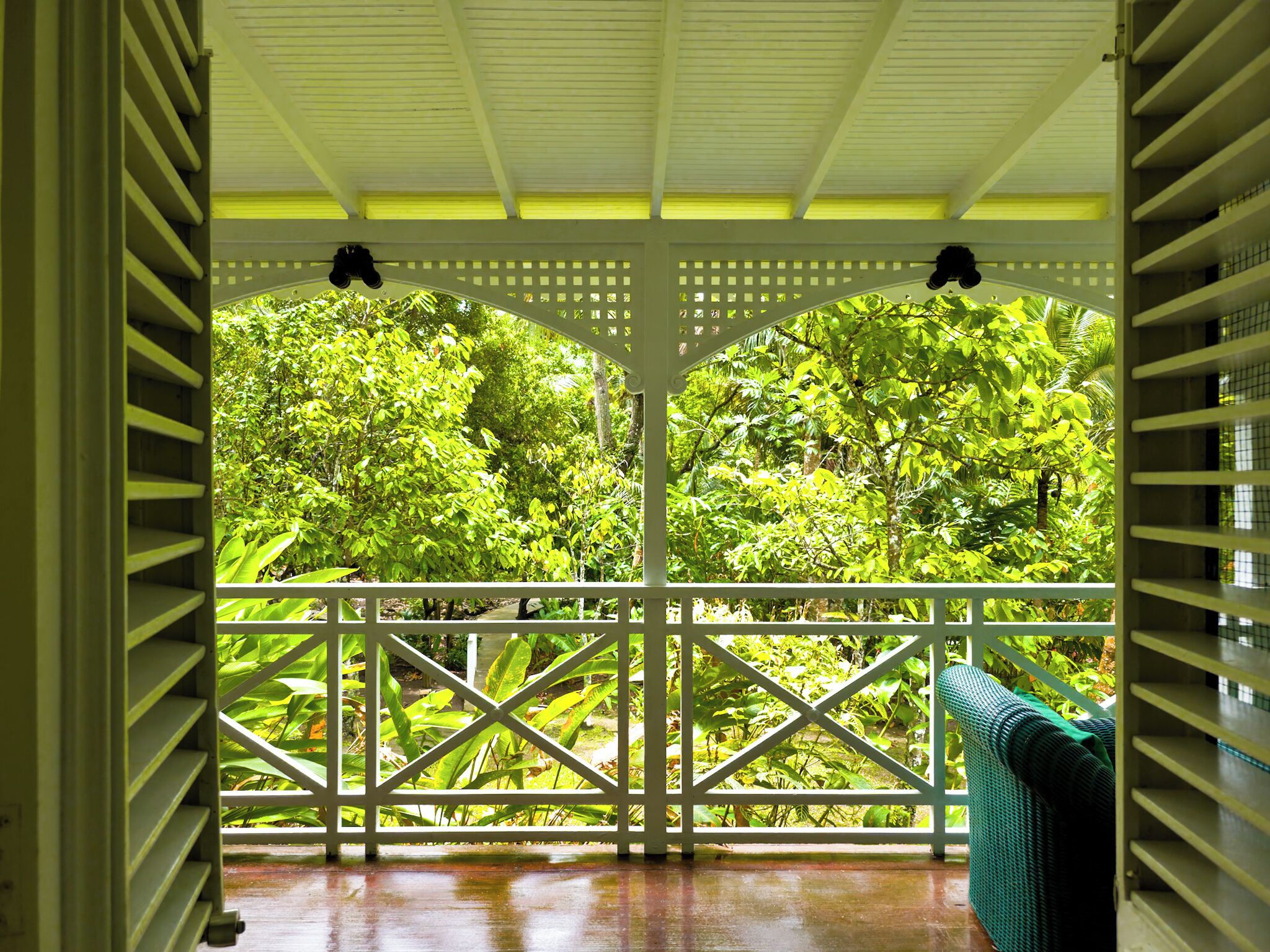 Un espacio al aire libre techado con piso de madera, baranda de celosía blanca y vistas a un follaje verde denso.