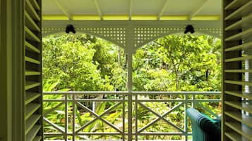 Un espacio al aire libre techado con piso de madera, baranda de celosía blanca y vistas a un follaje verde denso.