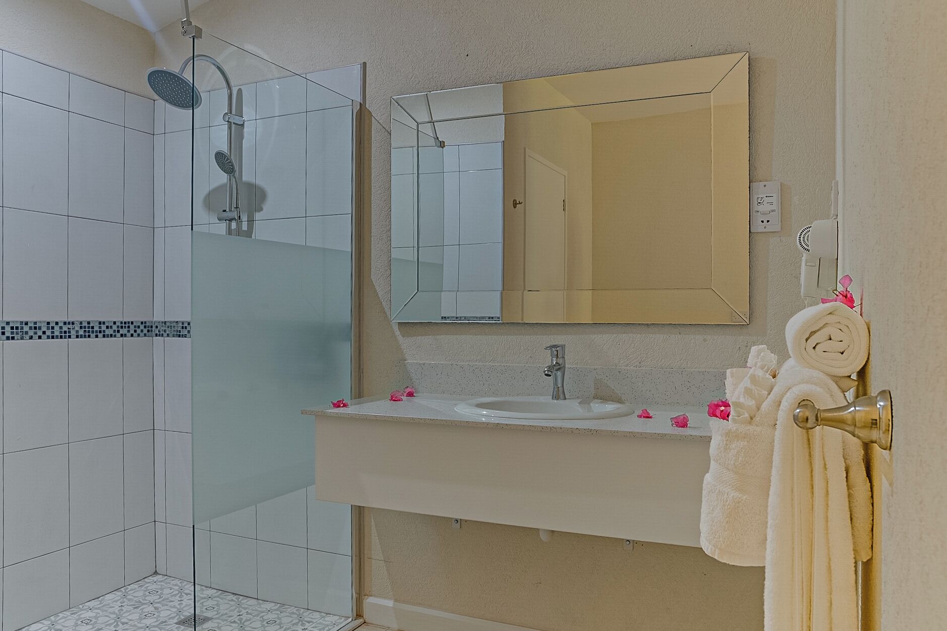 A bathroom with a shower, a sink, a mirror, and a towel rack.