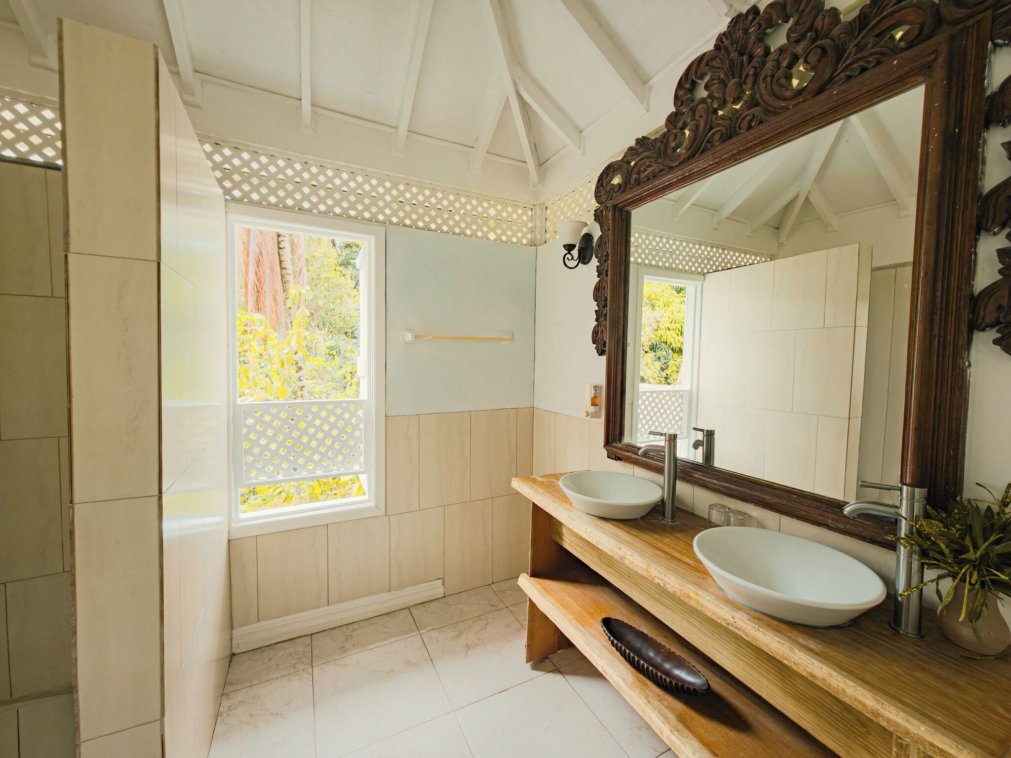 A bathroom with two sinks, a wooden vanity, a large mirror, and a window with a view of greenery.