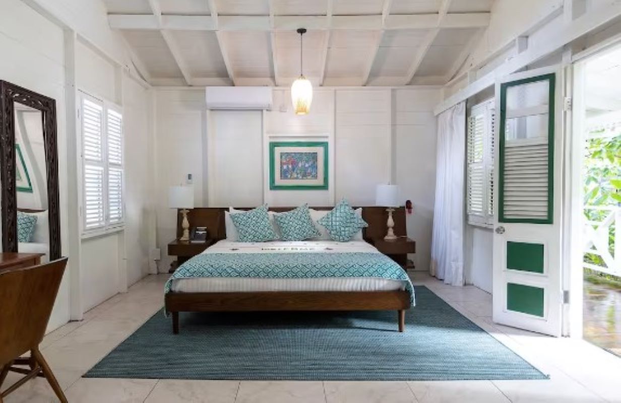 A bedroom with a bed, bedside tables, a hanging light, a framed picture on the wall, and a door with shutters.