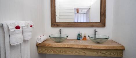A bathroom with a wooden vanity, two glass sinks, and a mirror above.