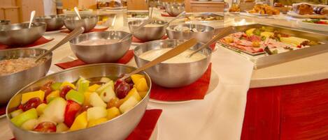 Un buffet proposant une variété de plats, notamment des fruits, des viandes et d’autres mets.