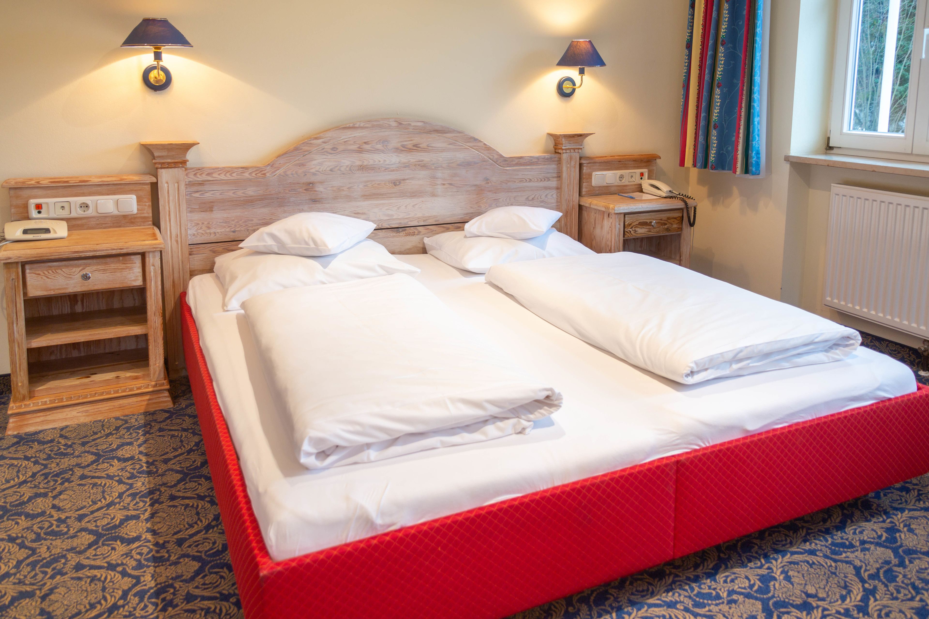 A double bed with white linens, two bedside tables with lamps, a wooden headboard, and a patterned carpet.
