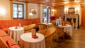 Un coin repas accueillant, avec un canapé rouge à motifs, des chaises en osier et des tables rondes dressées pour le repas.