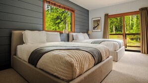 Une chambre avec deux lits, une grande fenêtre donnant sur les arbres et un tableau encadré au mur.