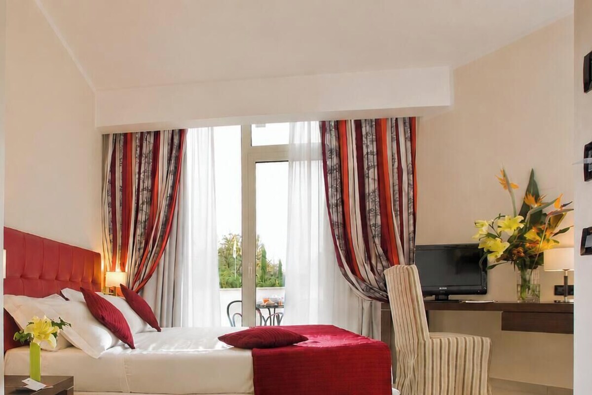 A hotel room with a bed, a desk with a TV, and a window with curtains.