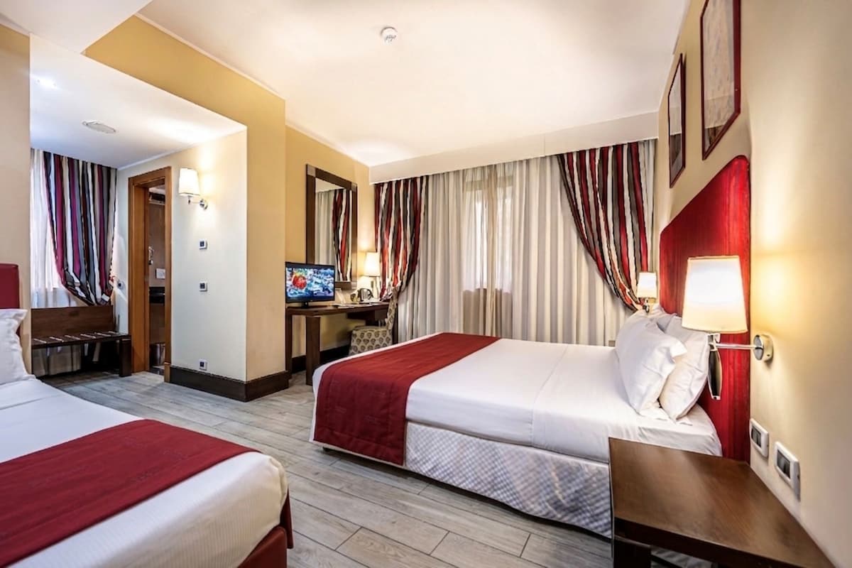 A hotel room with two beds, a desk, a television, and a bathroom.