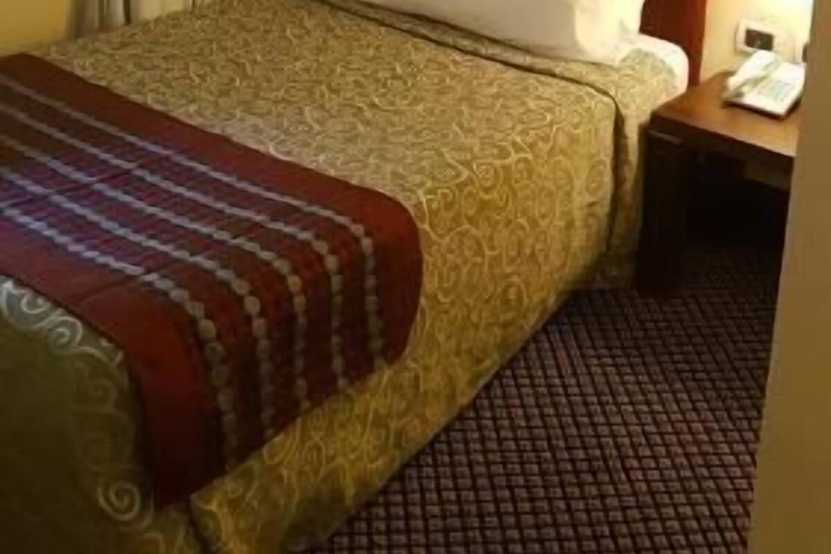 Ein Hotelzimmer mit Bett, Vorhängen, einem Nachttisch und einer Lampe.