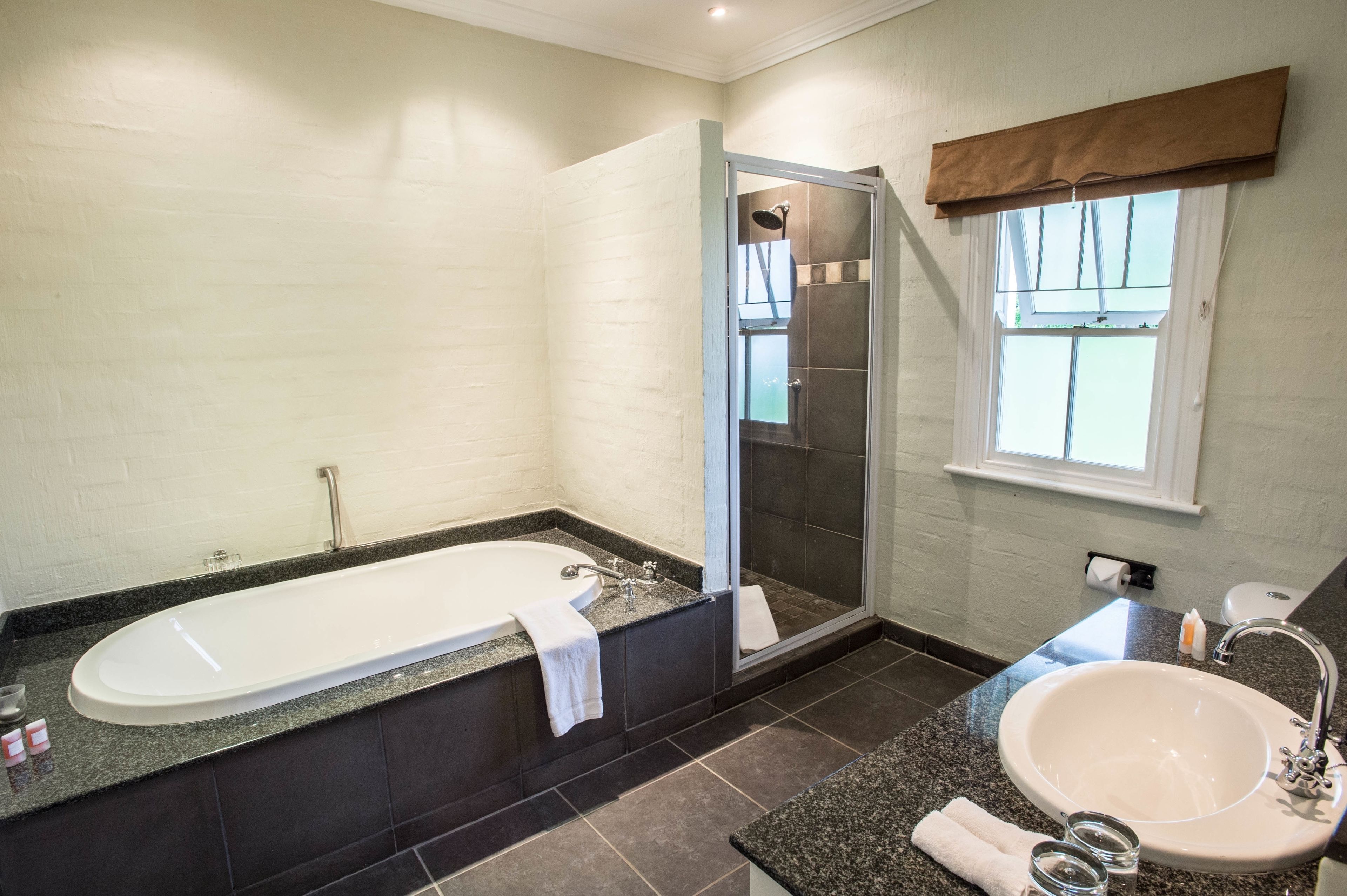 A modern bathroom with a freestanding bathtub, a glass-enclosed shower, a sink, and a window with a brown valance.