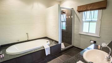 A modern bathroom with a freestanding bathtub, a glass-enclosed shower, a sink, and a window with a brown valance.