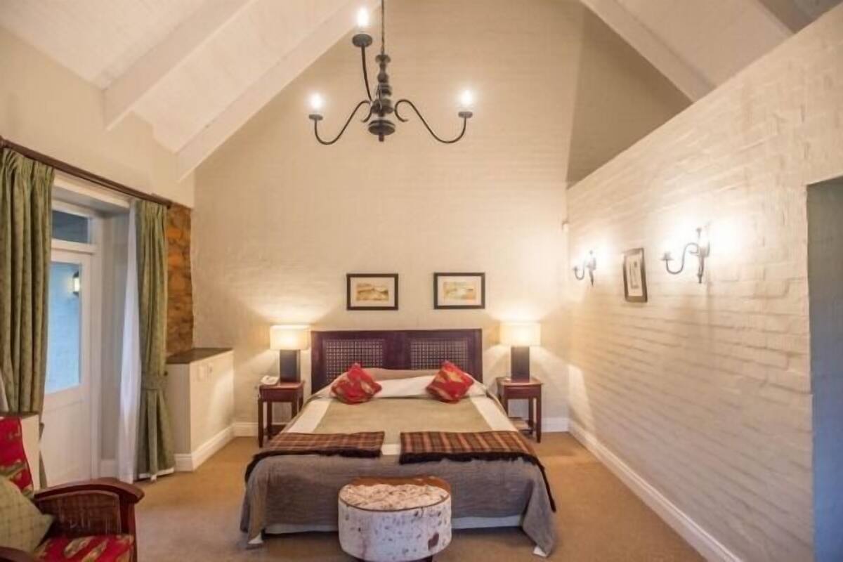 A bedroom with a large bed, two bedside tables, a chandelier, and a window with curtains.