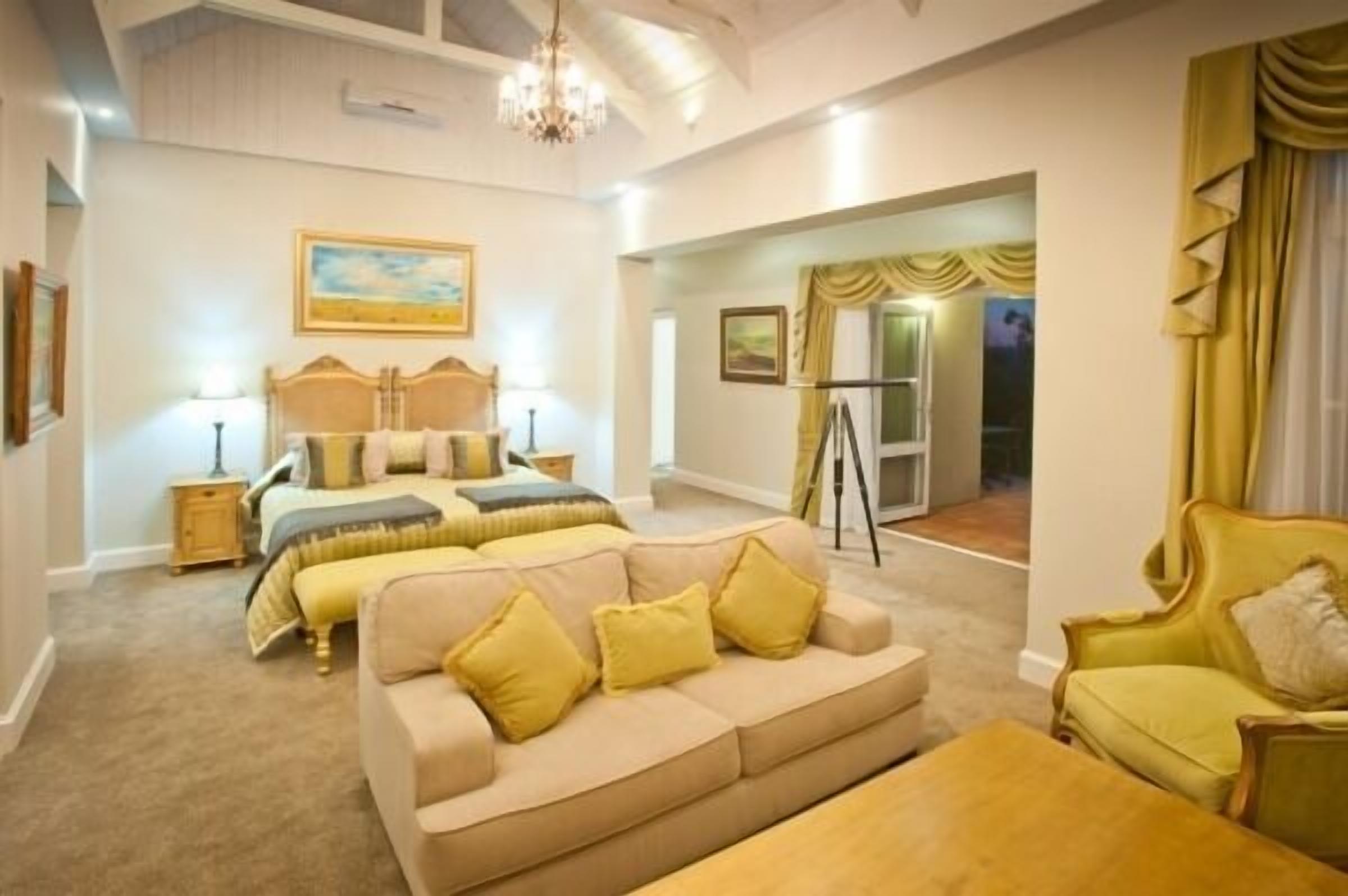 A bedroom with a large bed, a sofa, and a desk. There is a window with curtains and a chandelier.