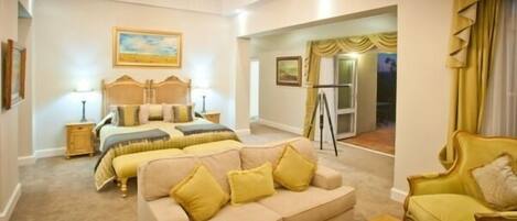A bedroom with a large bed, a sofa, and a desk. There is a window with curtains and a chandelier.