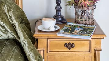 Una mesita de noche de madera con una lámpara, un florero con flores, una revista y una taza de café.