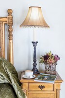 Una mesita de noche de madera con una lámpara, un florero con flores, una revista y una taza de café.