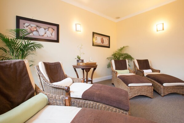 A spa room with wicker chairs, a small table with a plant, and framed artwork on the walls.
