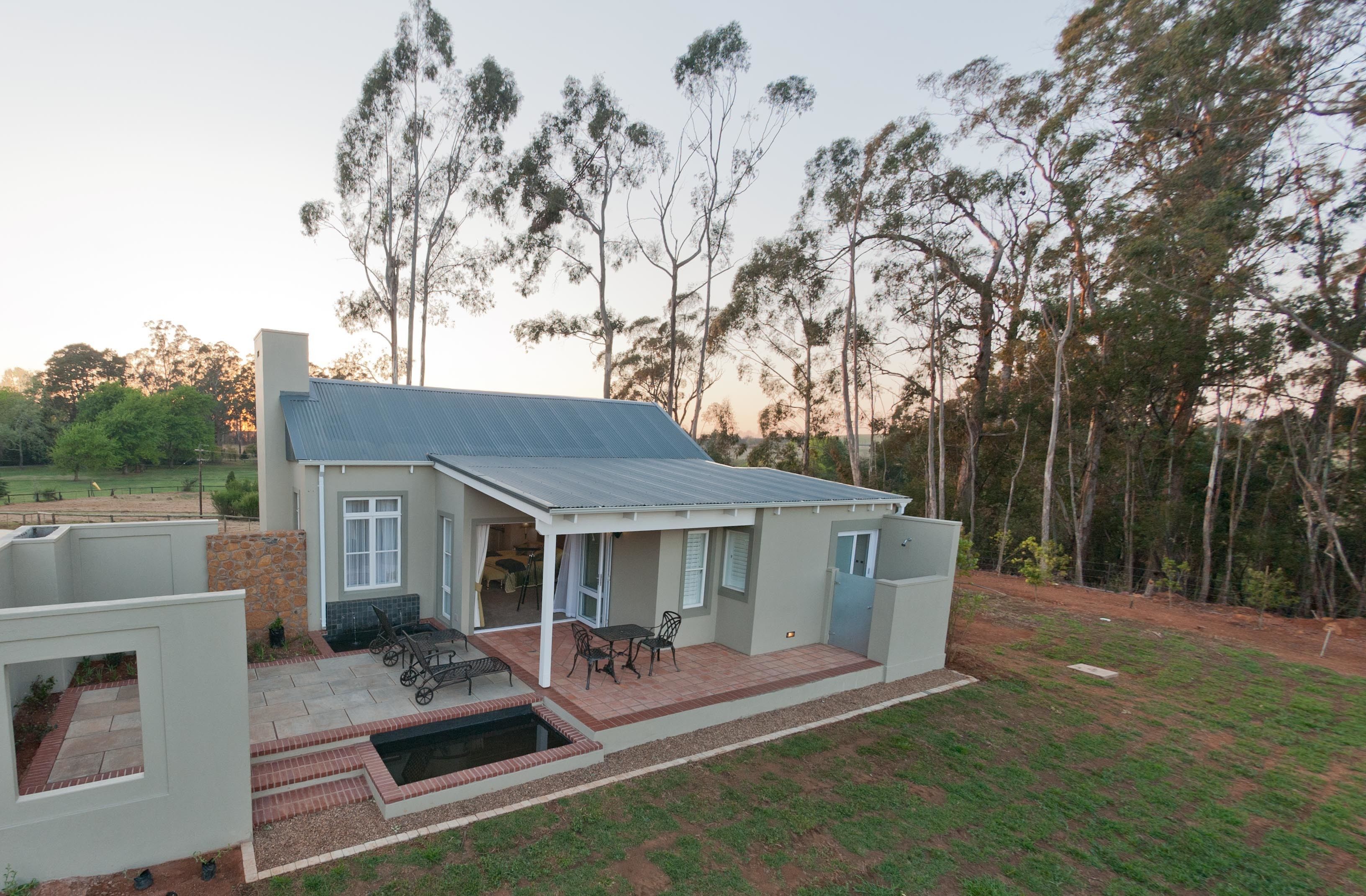 A modern house with a patio, a swimming pool, and a view of the surrounding trees.