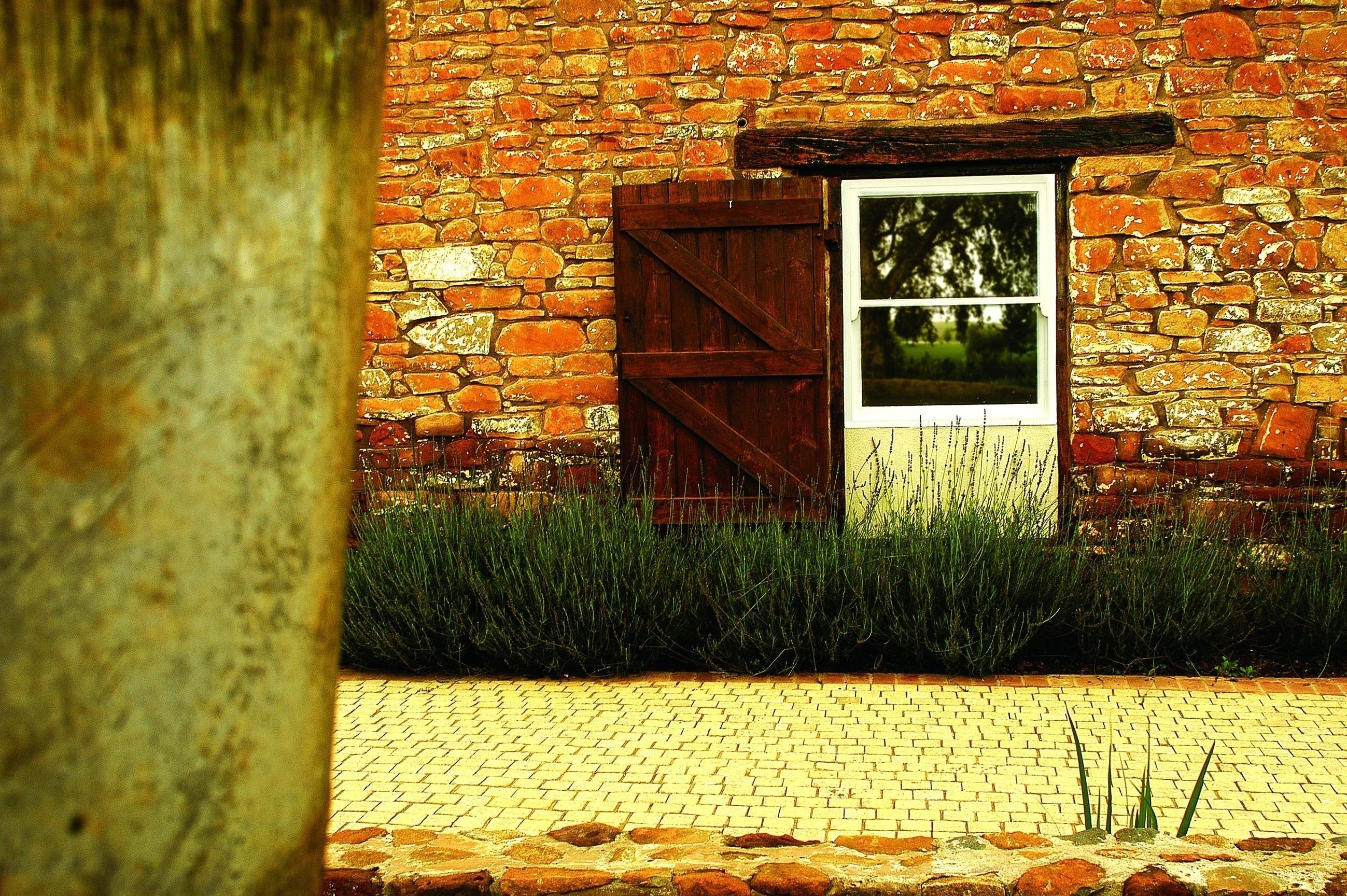 A brick building with a wooden door and window, surrounded by grass and a cobblestone path.