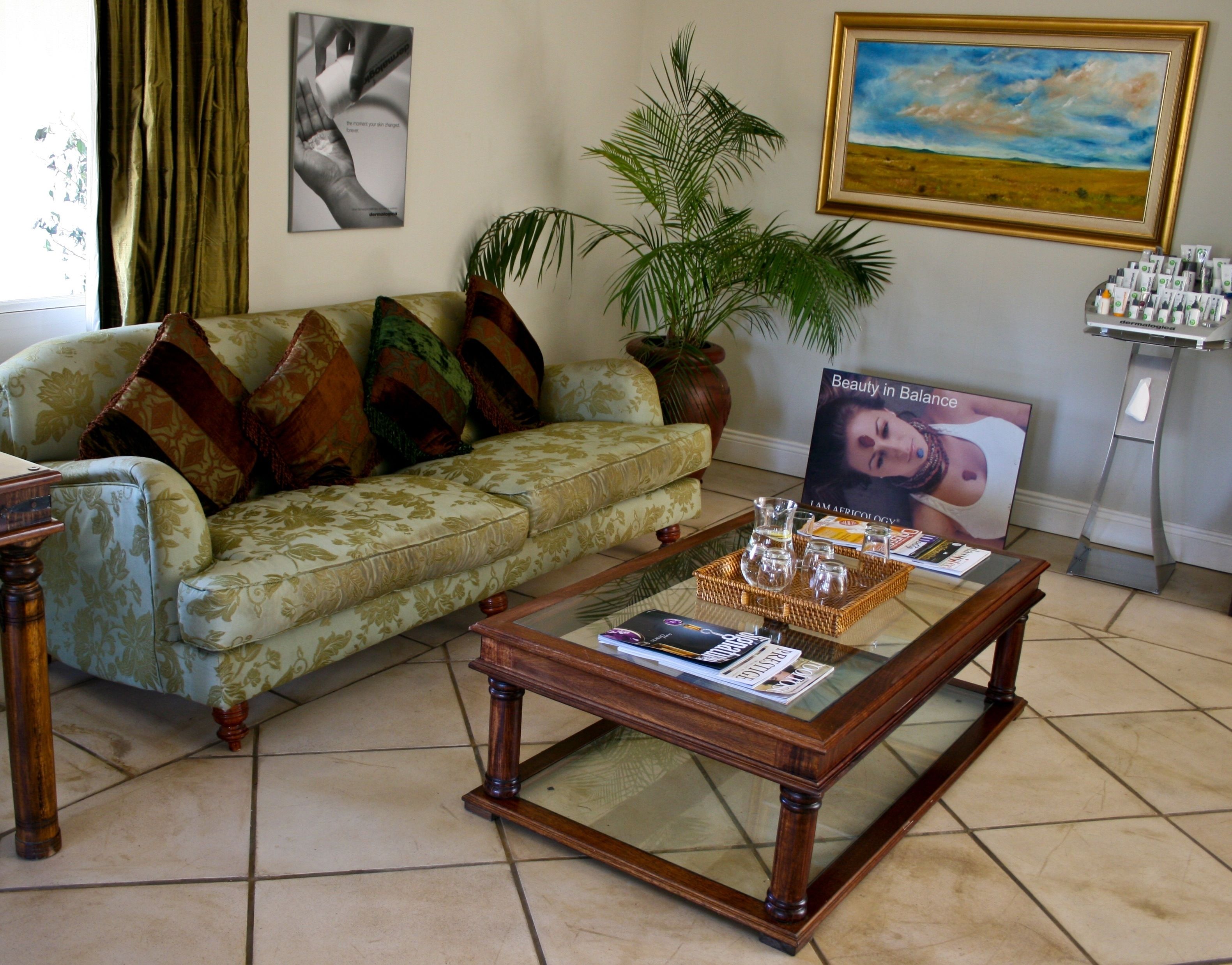 A living room with a green sofa, a wooden coffee table with magazines, a potted plant, and a framed landscape painting.