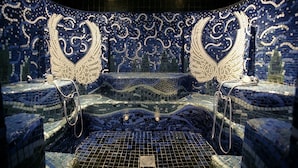 Une baignoire recouverte de mosaïques, dotée de deux pommes de douche et d’un drain.
