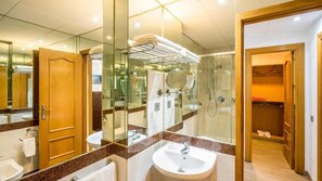 A modern bathroom with a glass shower enclosure, a wooden door, and a walk-in closet with a mirror.