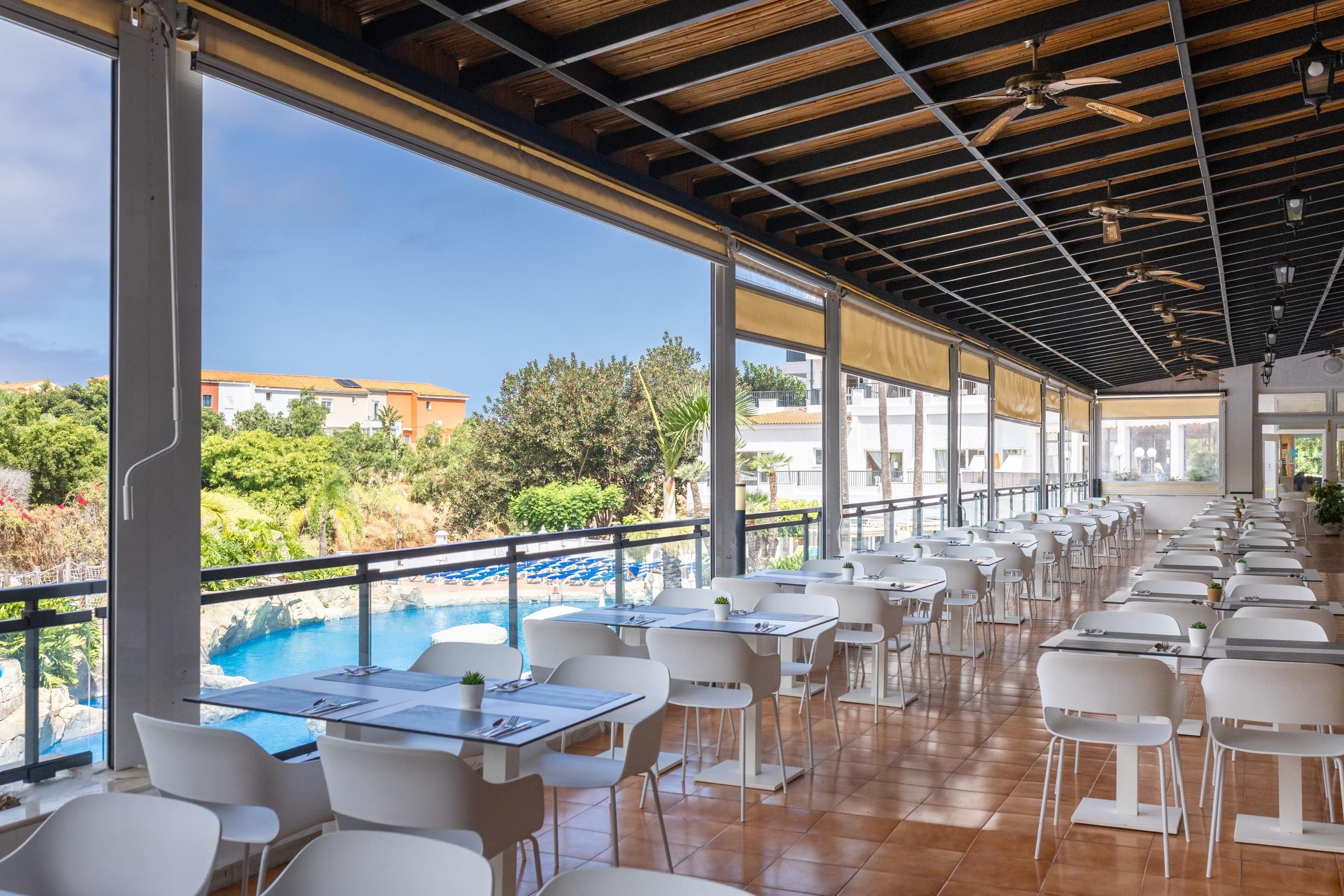 Un restaurante con terraza al aire libre con vistas a una piscina y follaje.